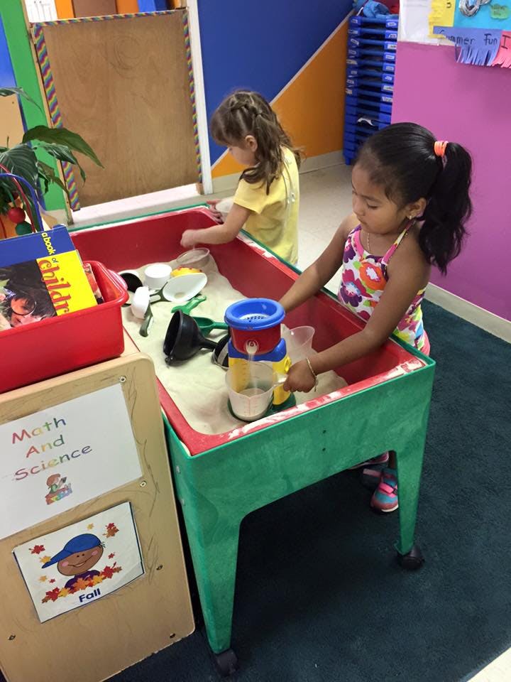 Two children playing at a sand table in a classroom