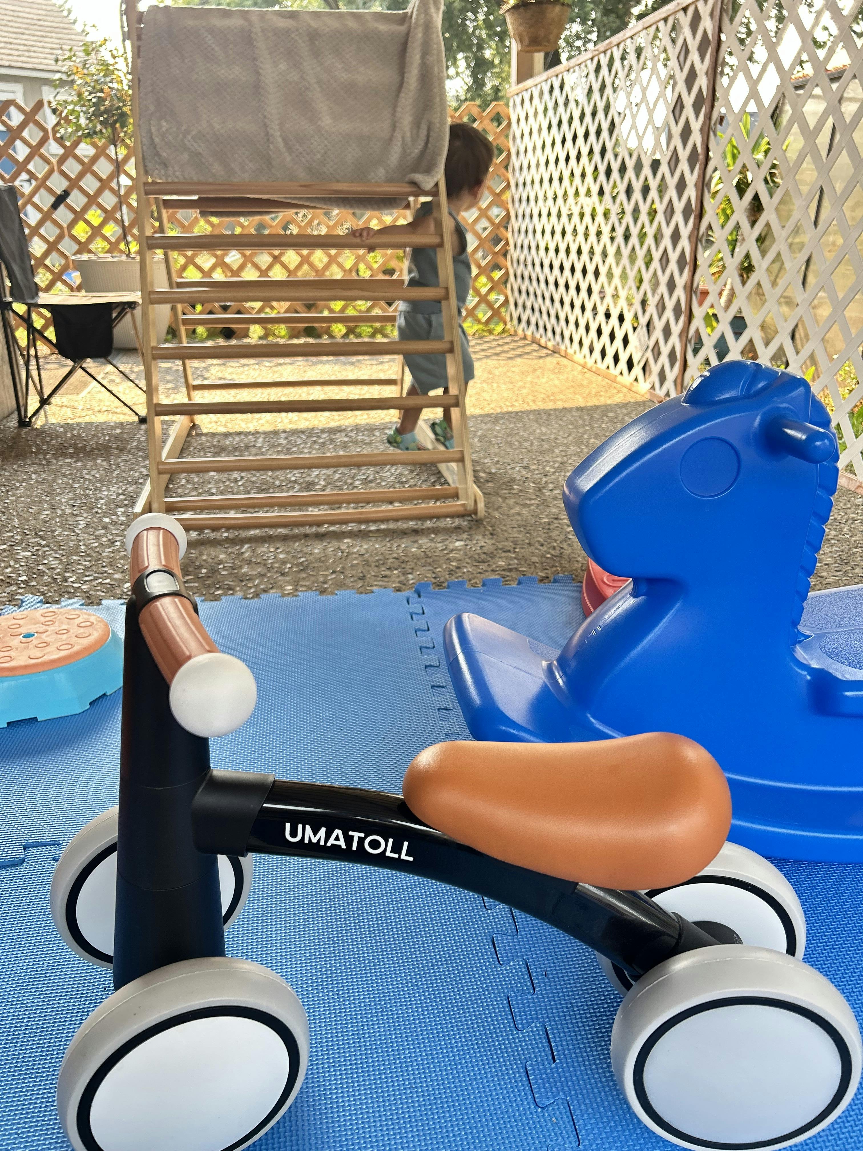 Child climbing on a wooden play structure near a toy bike and a rocking horse