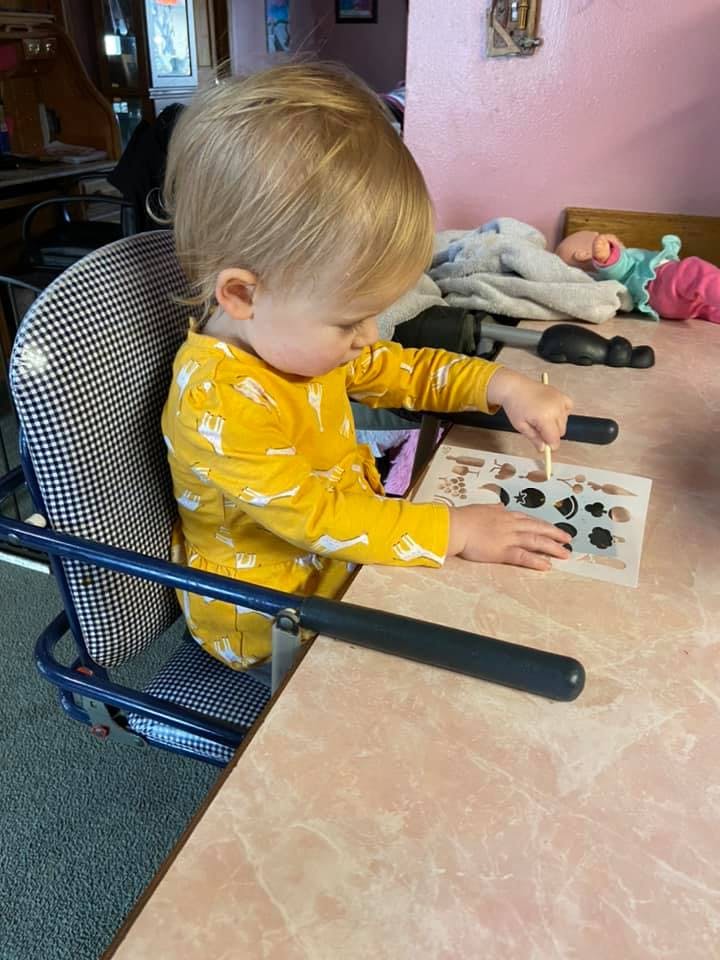 Child in a high chair playing with a stencil and stick on a table