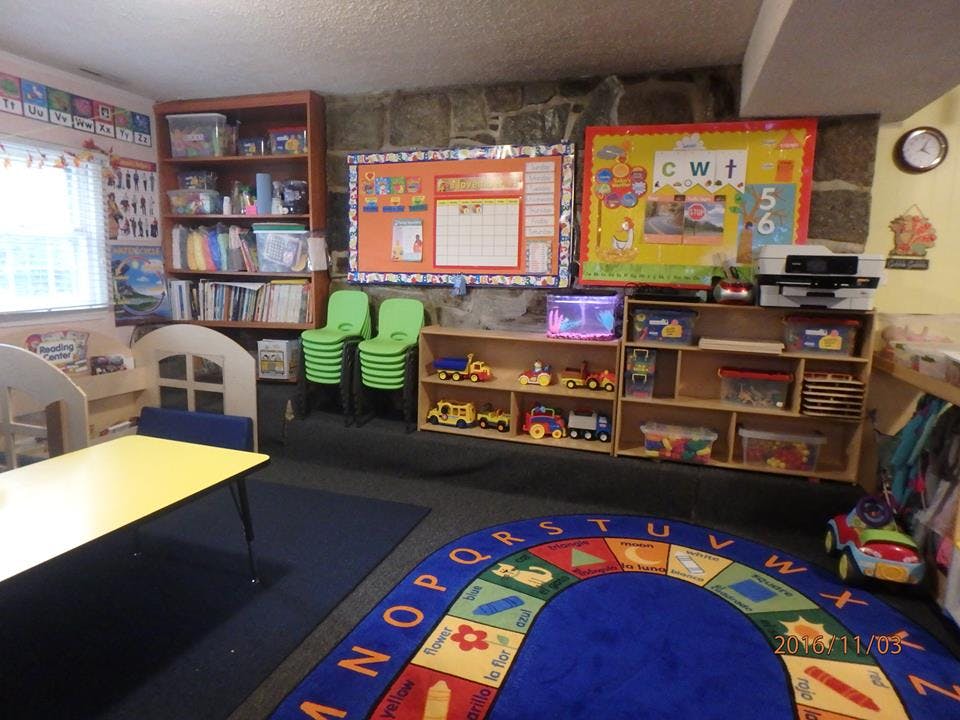 Classroom with a colorful alphabet rug, shelves of toys, and a yellow table