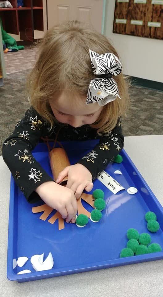 Child working on a craft project with a paper tree and green pom-poms