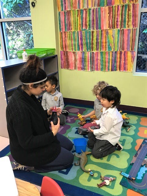 Person and three children playing with toys on a colorful rug in a classroom