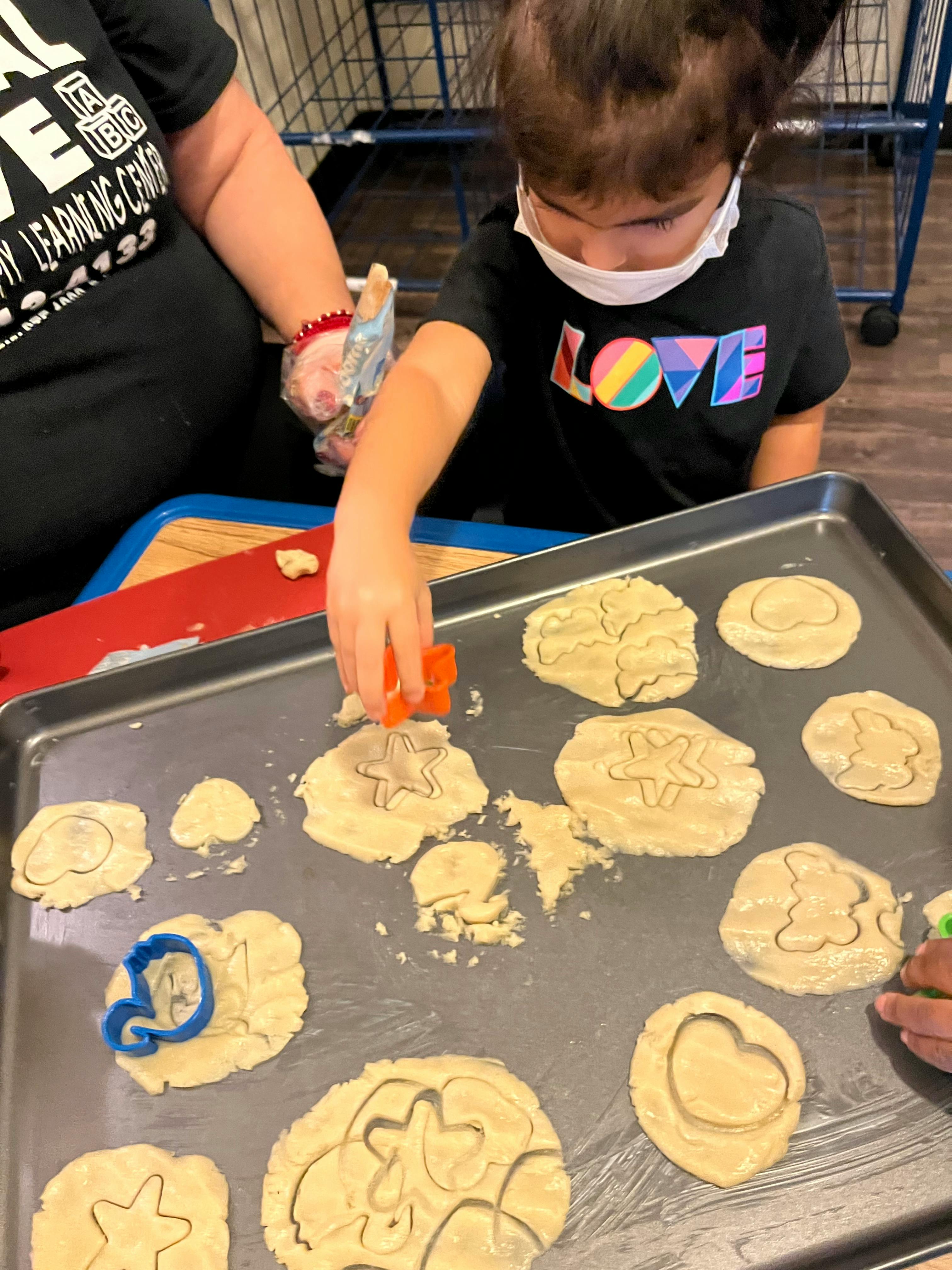 Child using cookie cutters on dough on a baking sheet