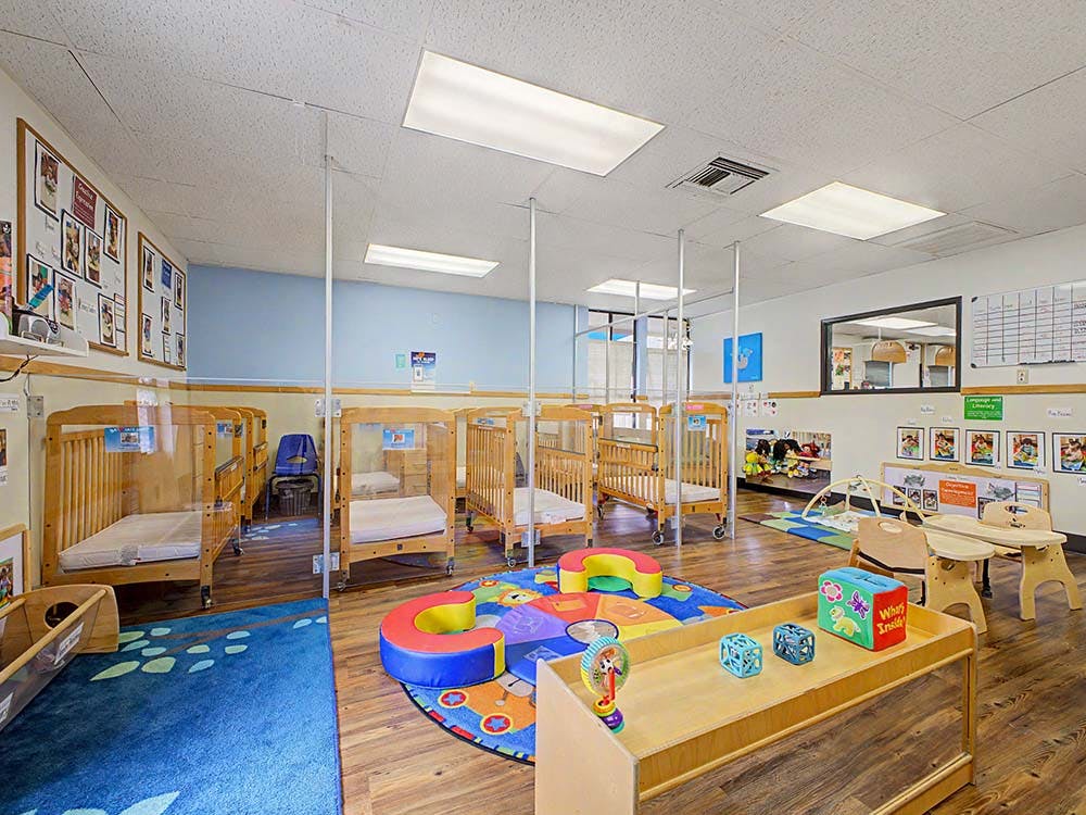 daycare classroom with multiple cribs, a play mat, and small tables