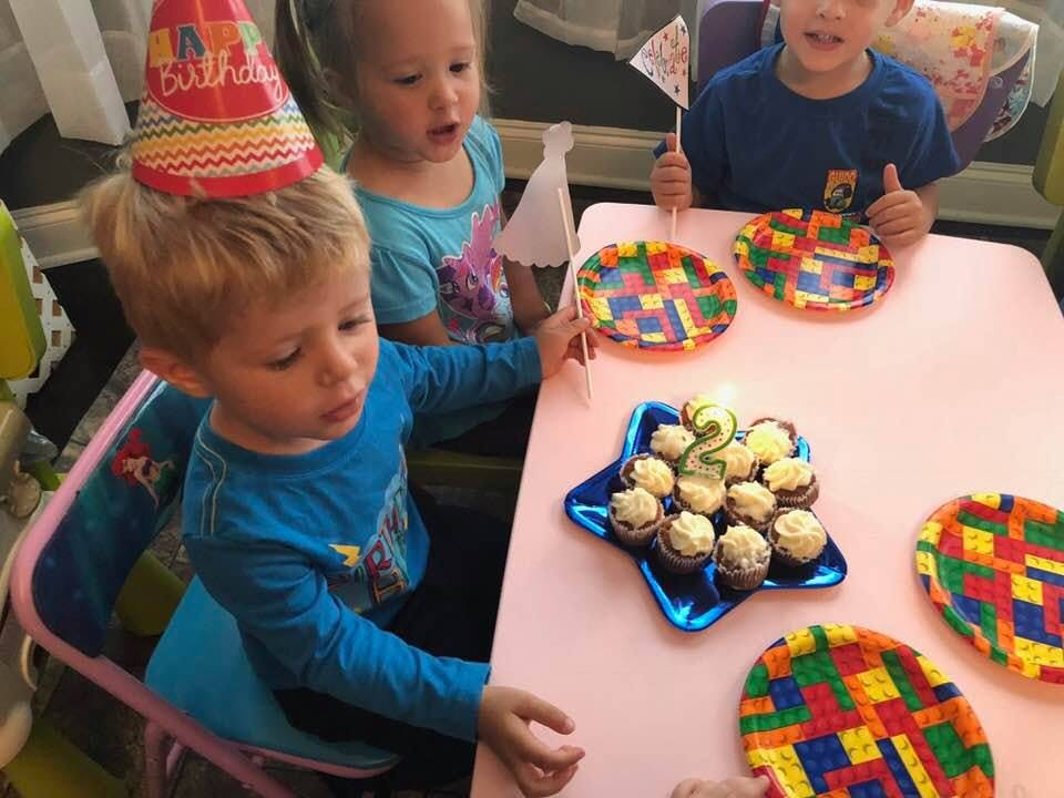 Child in a party hat looking at cupcakes with a lit candle