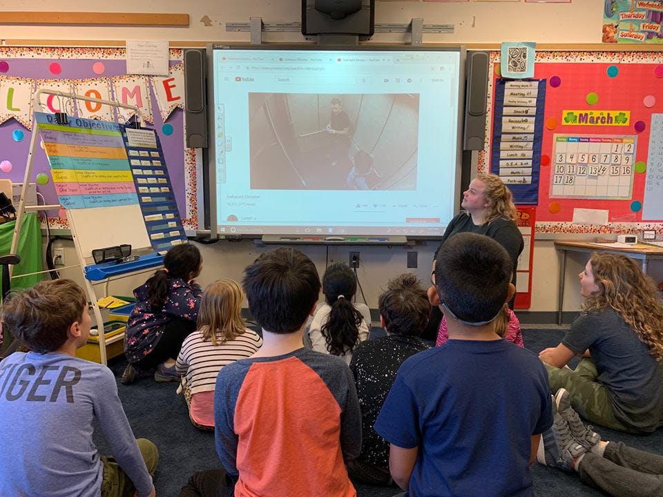 Teacher and children sitting on floor looking at a screen in a classroom