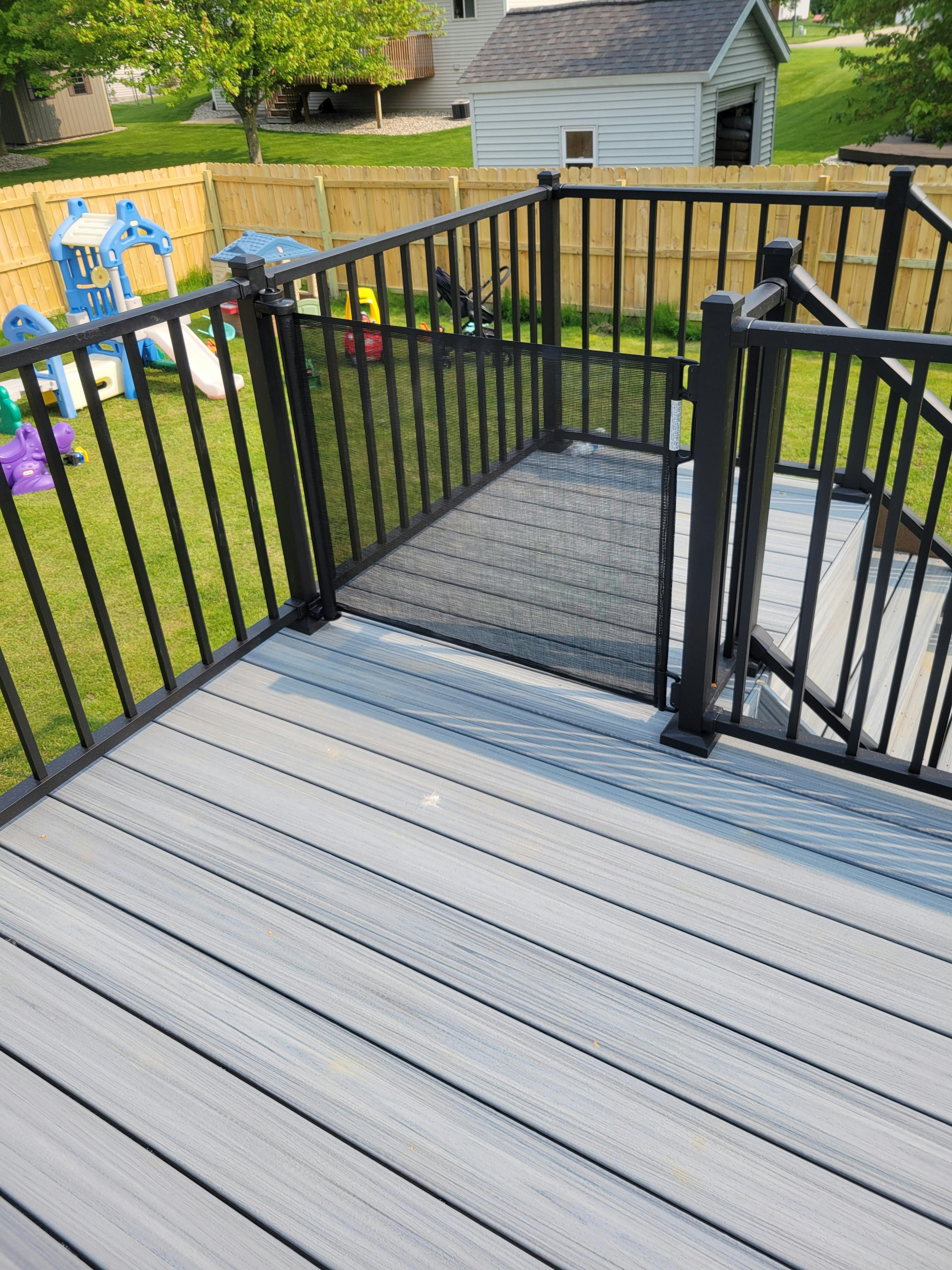 Deck with black railing overlooking a backyard with a wooden fence and playset