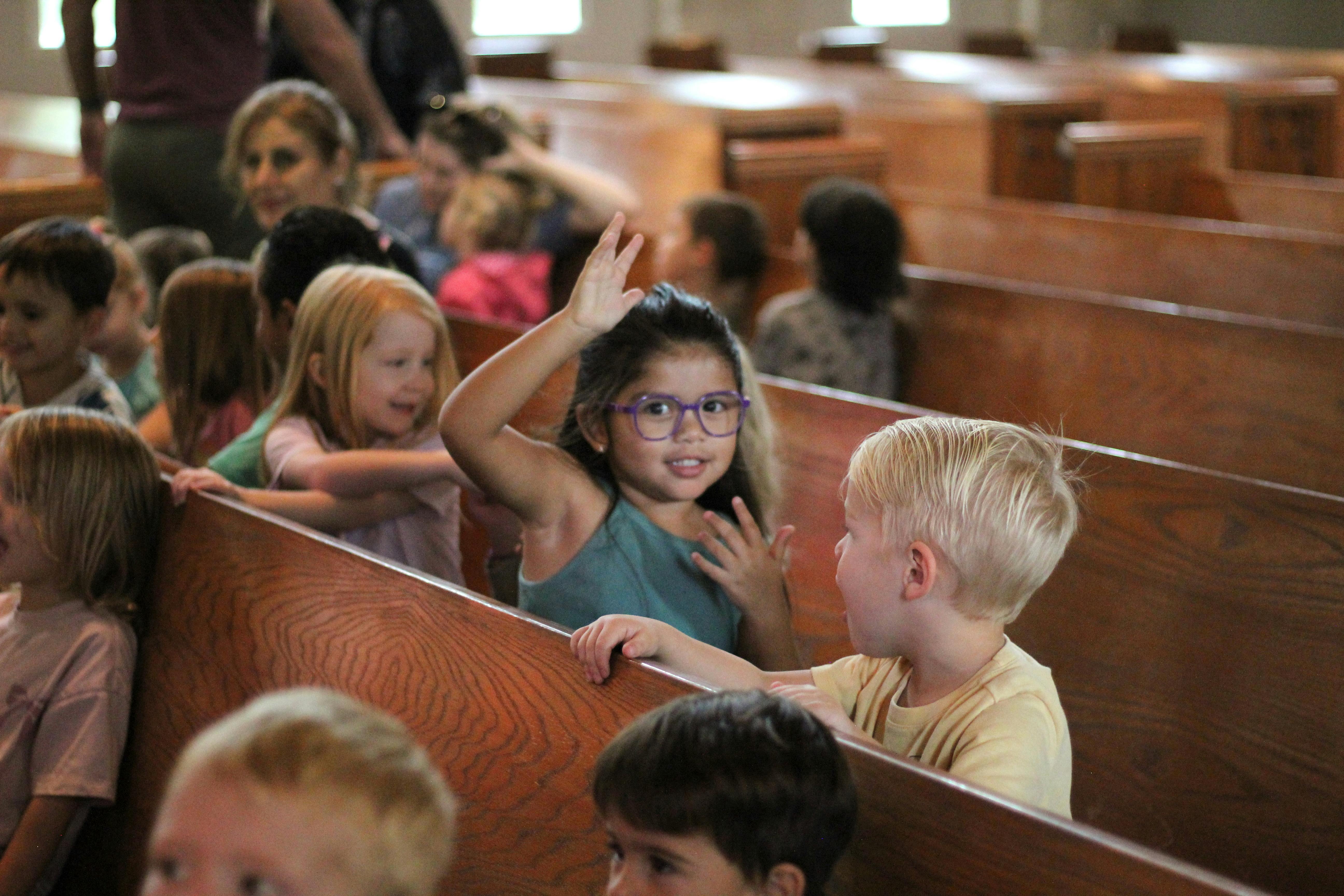 Child in purple glasses raising hand, another child looking at them