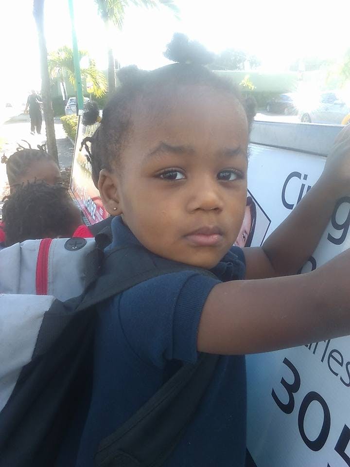Child wearing a blue shirt and backpack, holding a sign