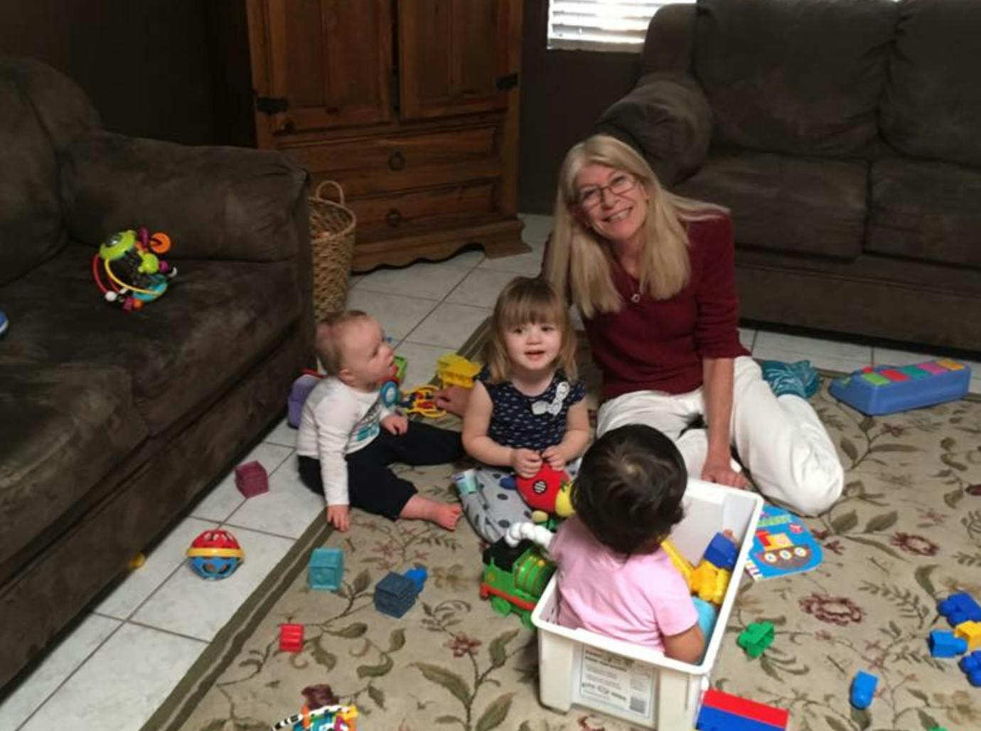 Adult and three children playing with toys on a rug