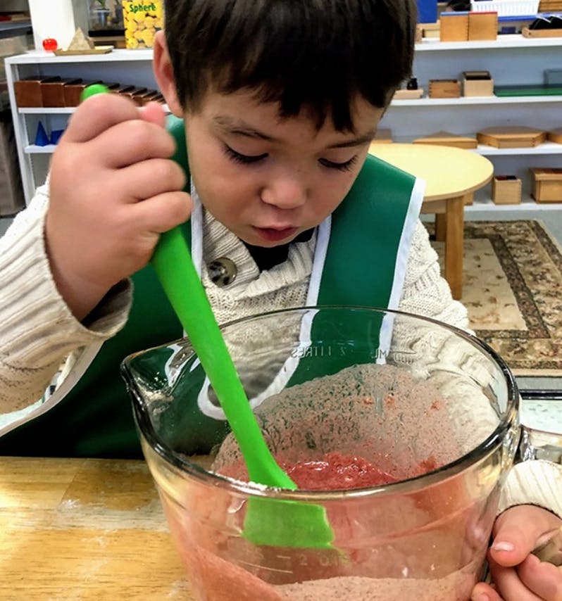 Child stirring a mixture in a bowl with a green spatula