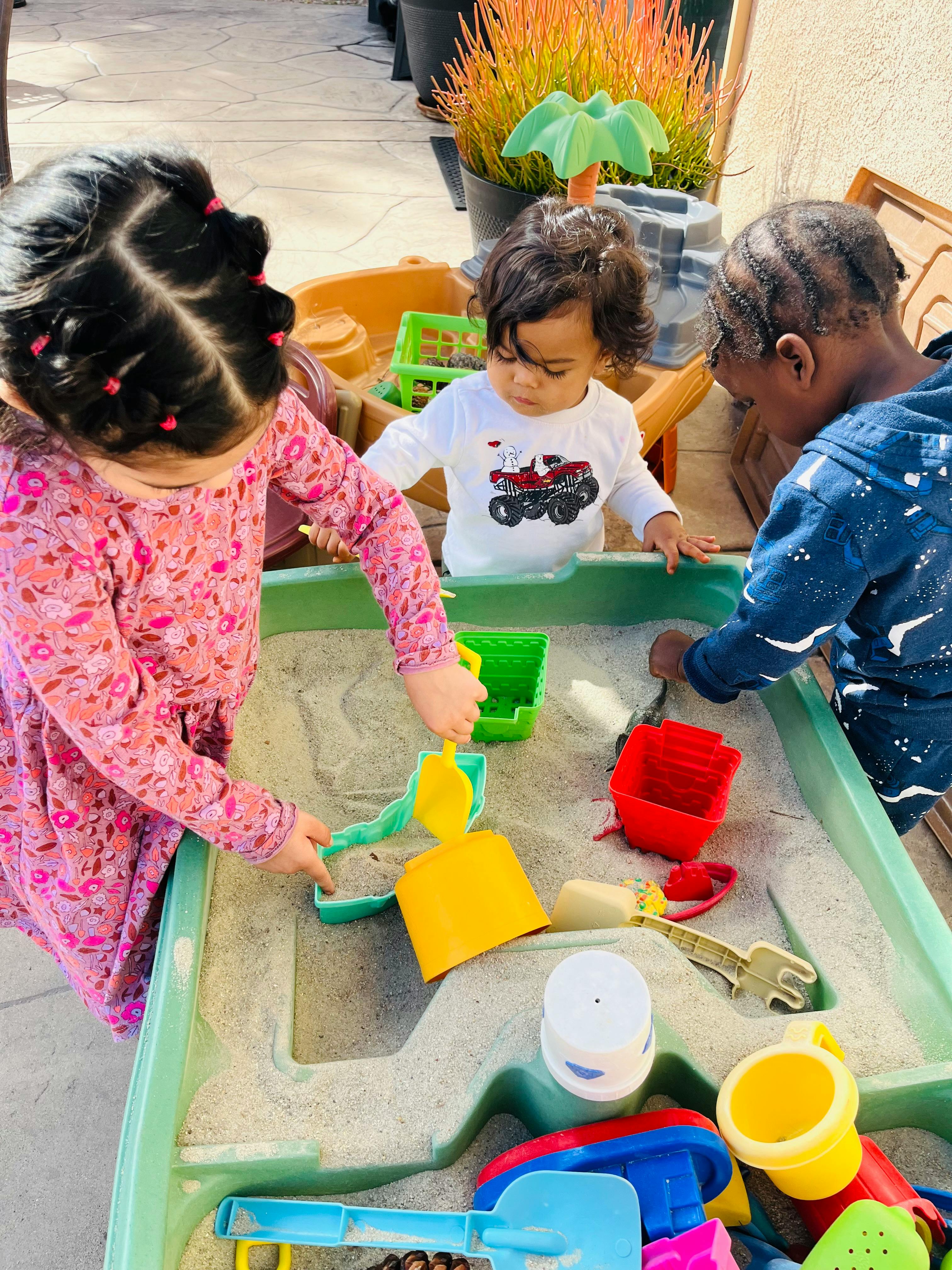 Three children playing in a sand table with toys