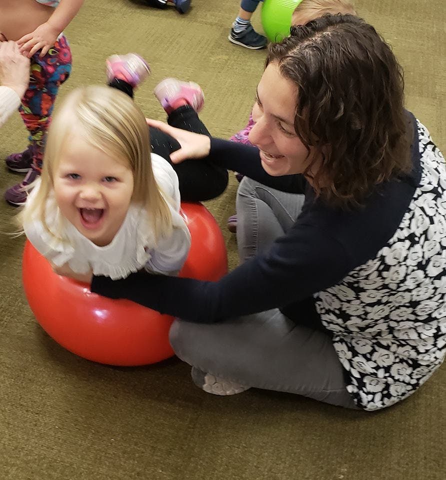 Person helping a child on a red exercise ball
