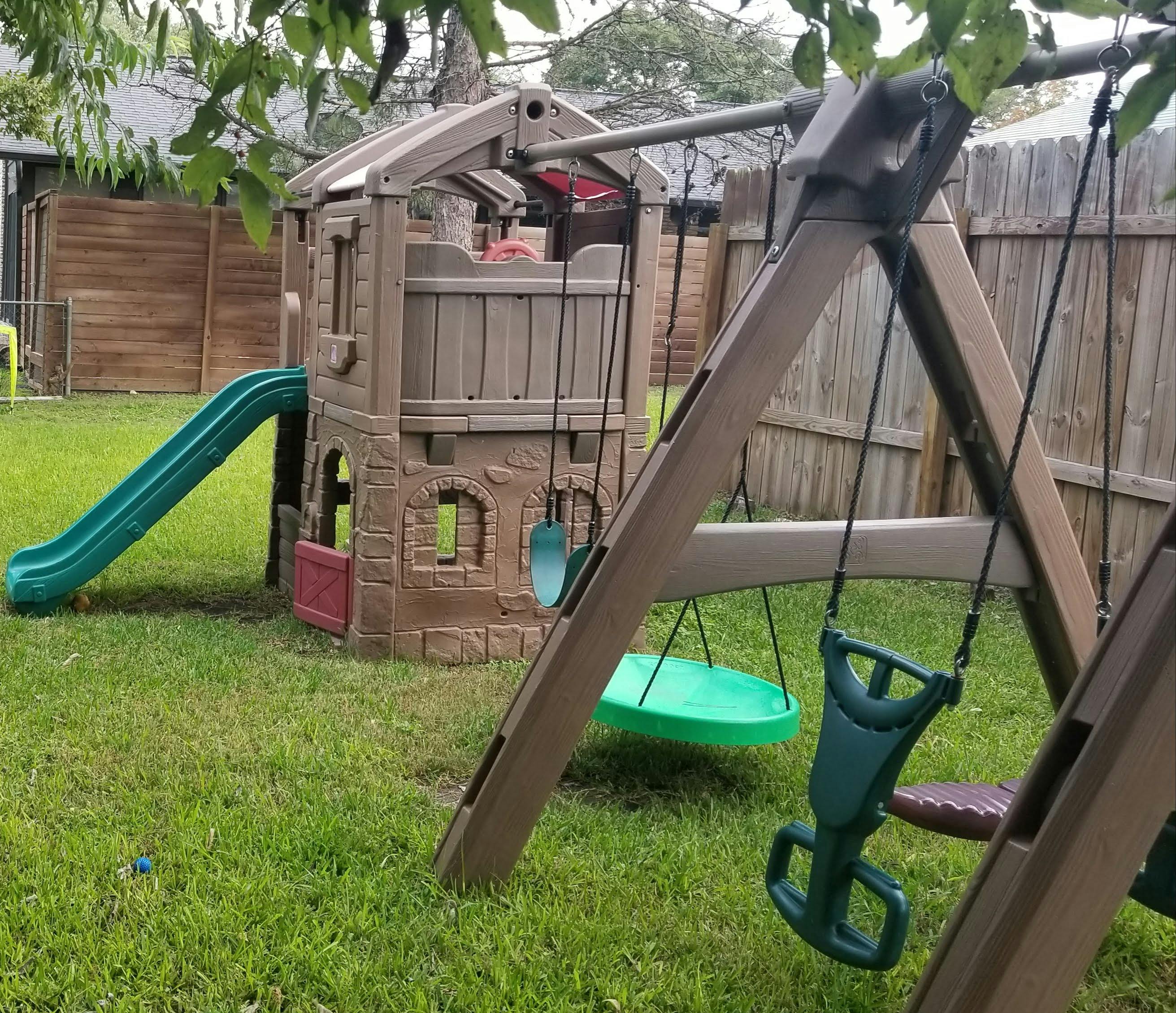 Plastic playground set with a slide and swings in a backyard