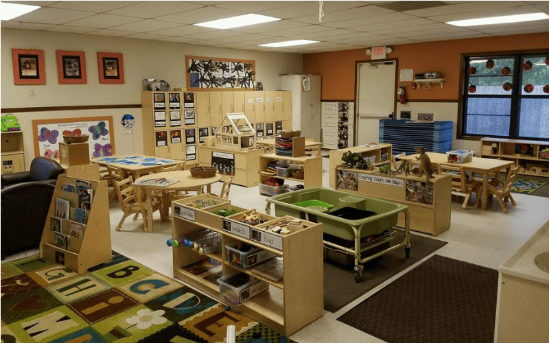 Classroom with small tables, chairs, shelving units, and a large alphabet rug