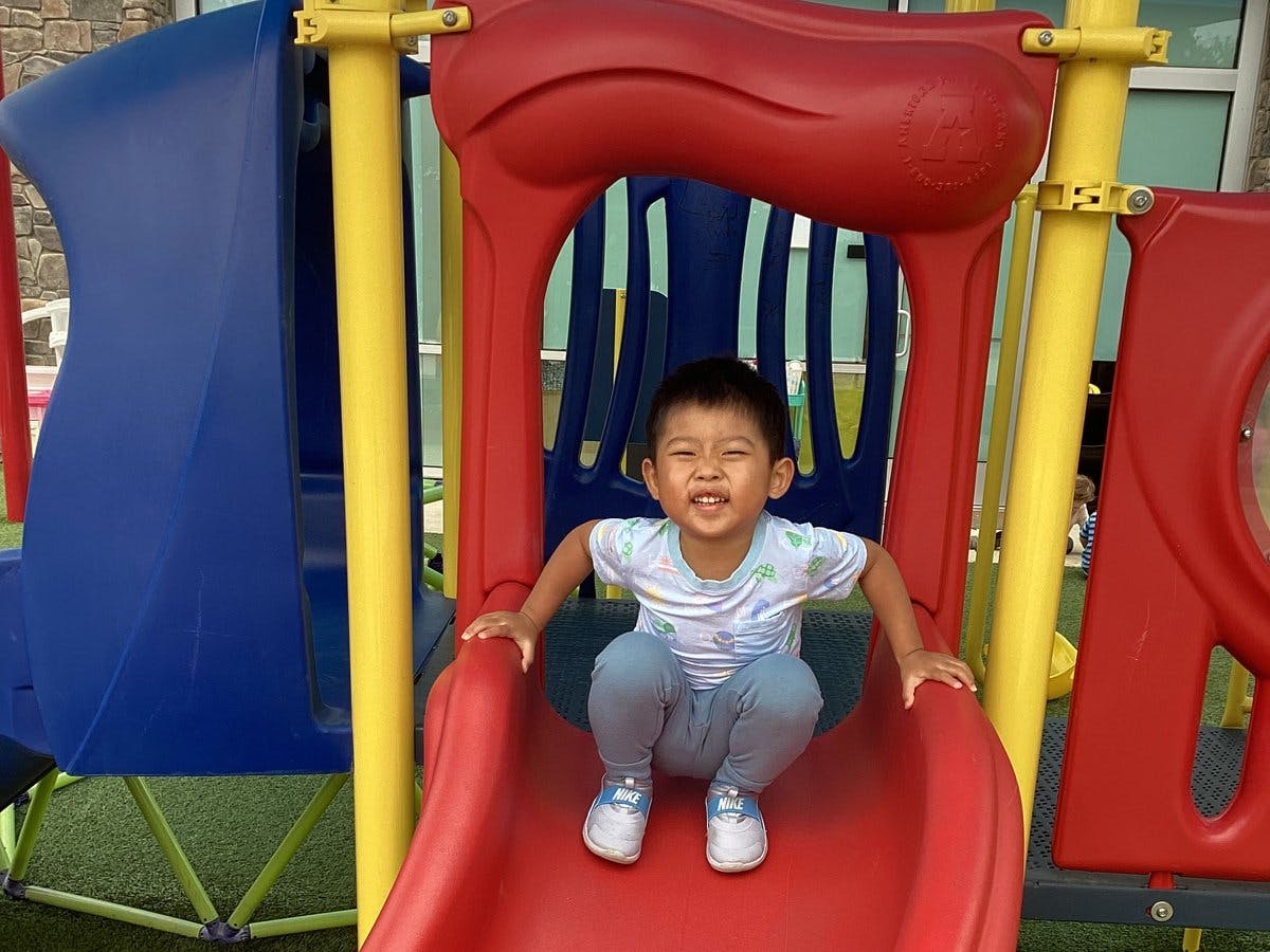 Child sitting at the top of a red playground slide