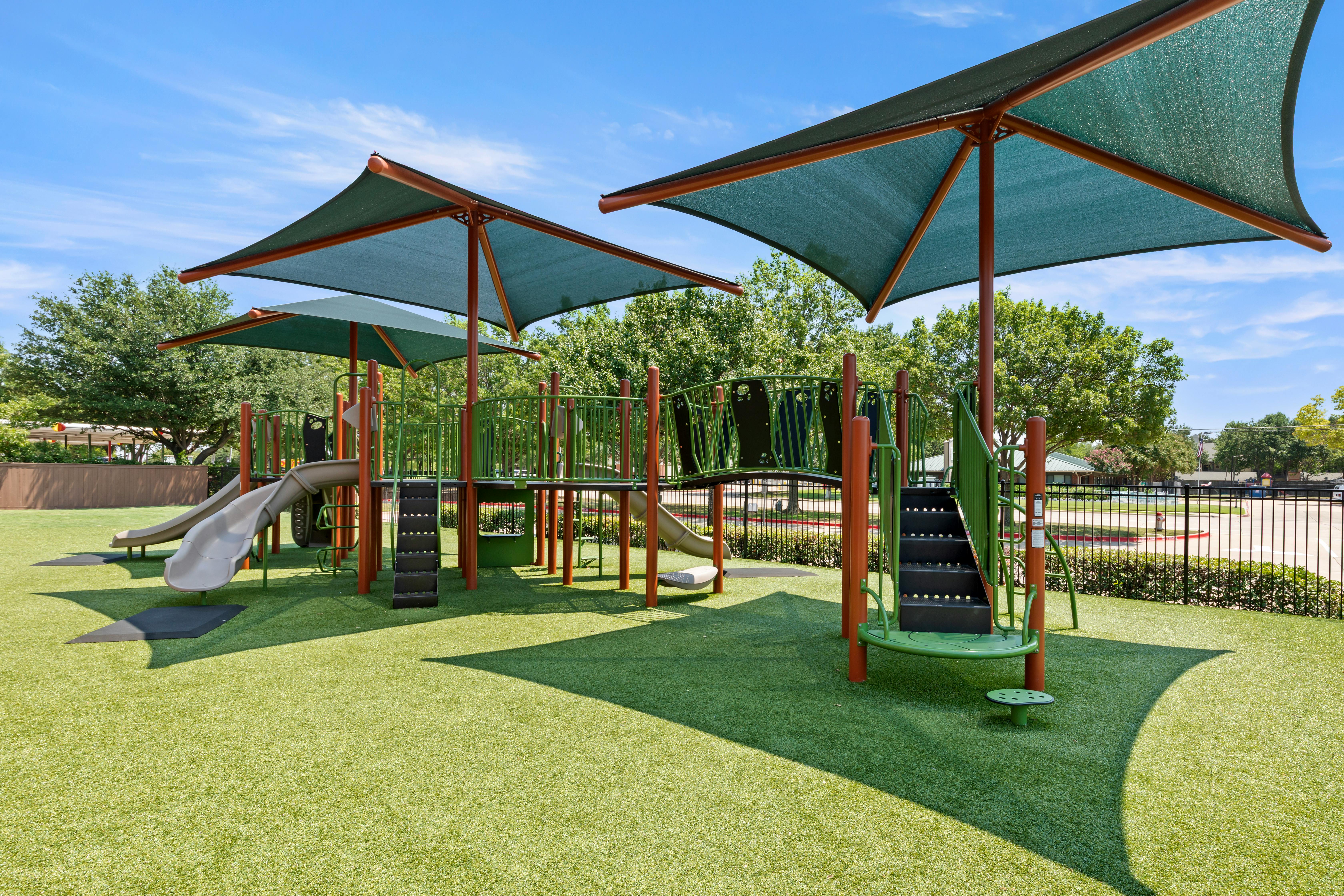 Empty children's playground with green artificial turf and shade canopies