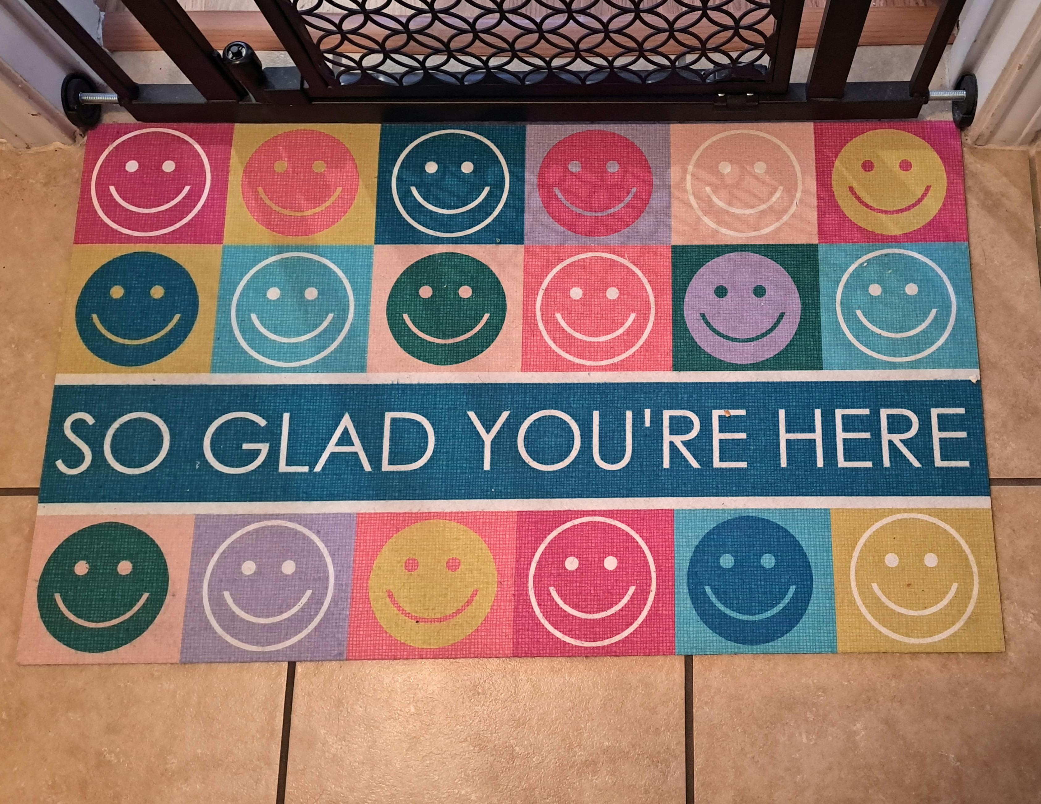 Doormat with colorful smiley faces and text "SO GLAD YOU'RE HERE"