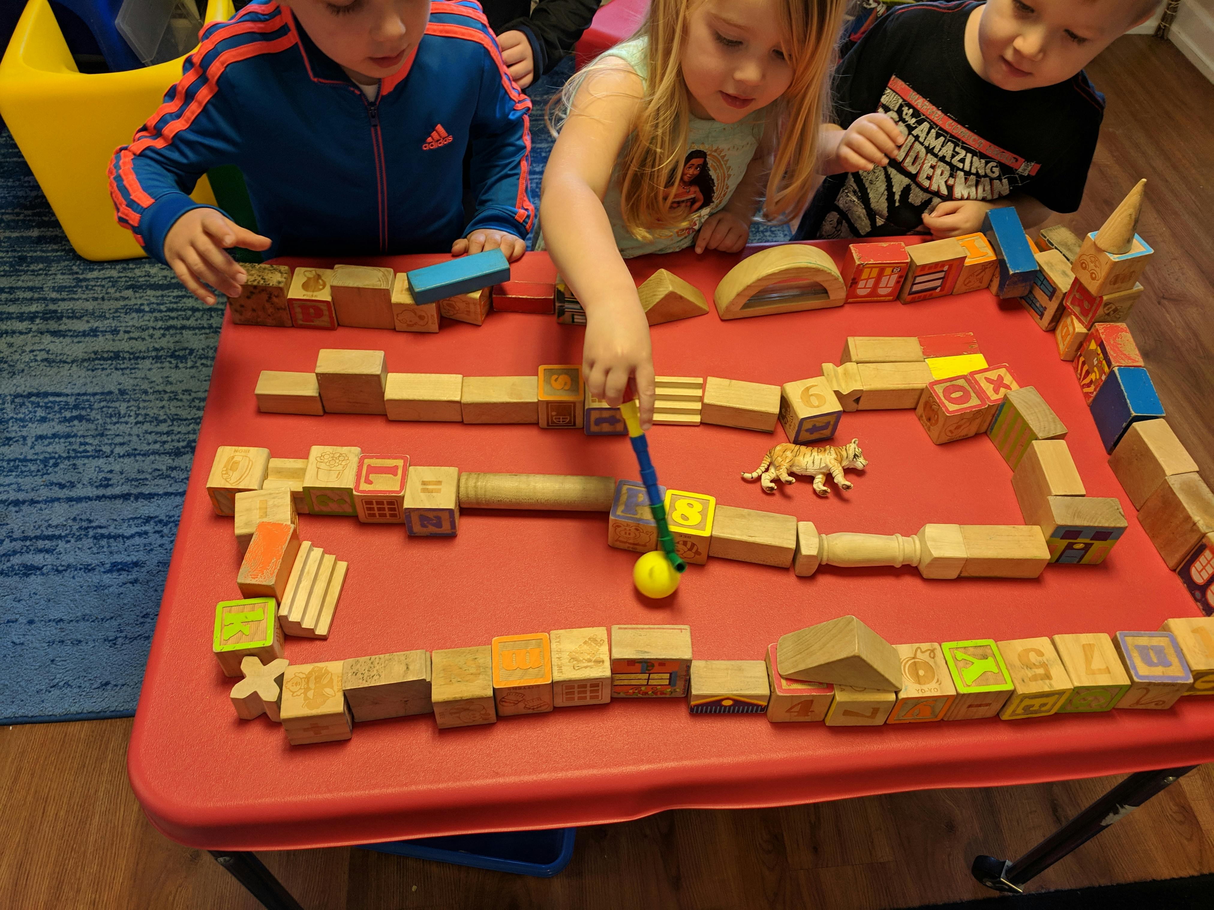 Children playing with wooden blocks on a red table