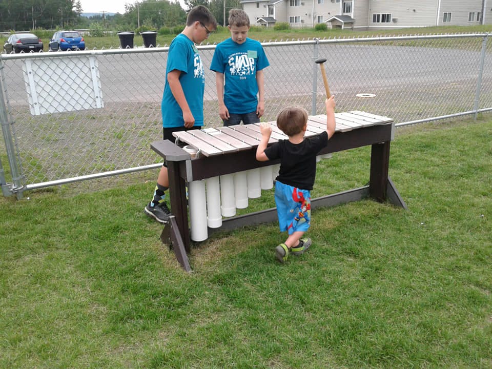Two teens and a child playing a large outdoor xylophone