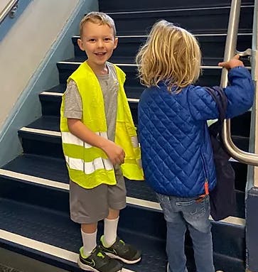 Two children on stairs, one wearing a safety vest