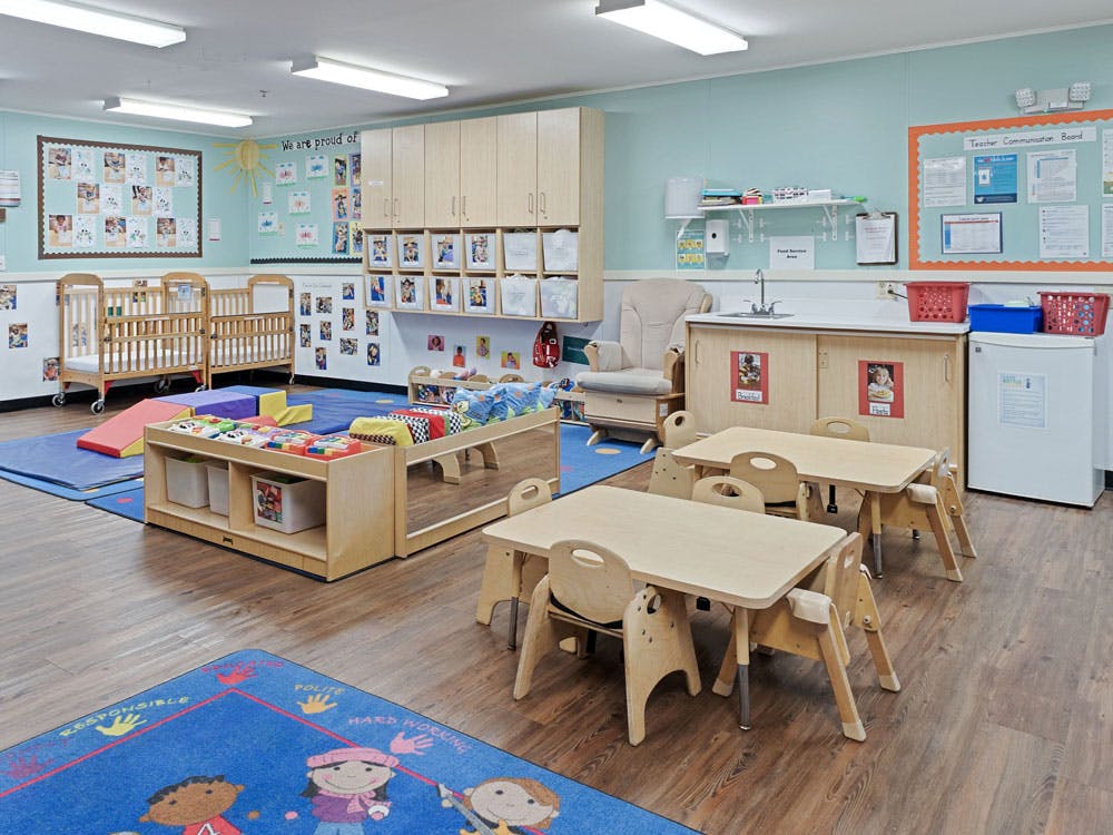 Classroom with cribs, play mats, small tables and chairs, and a sink area