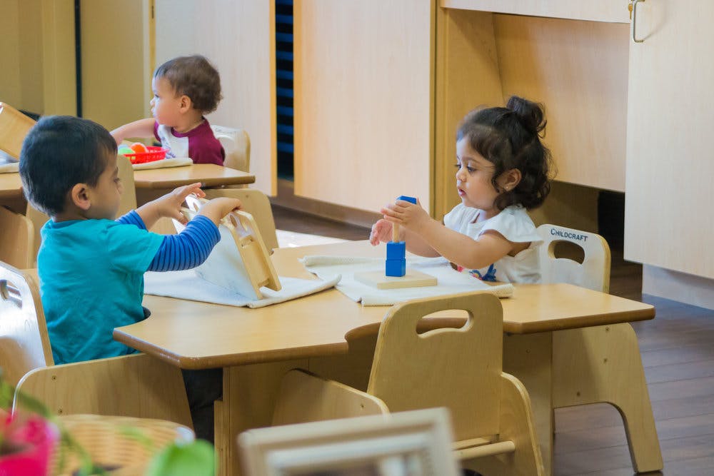Children playing with toys at small tables in a classroom