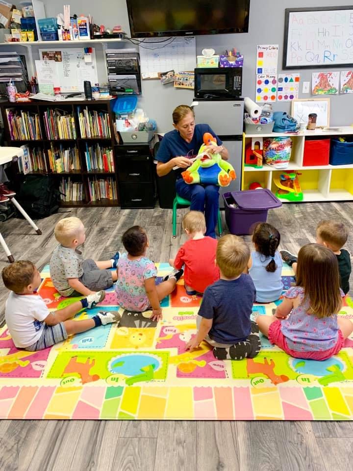 Adult showing a toy to children sitting on a mat