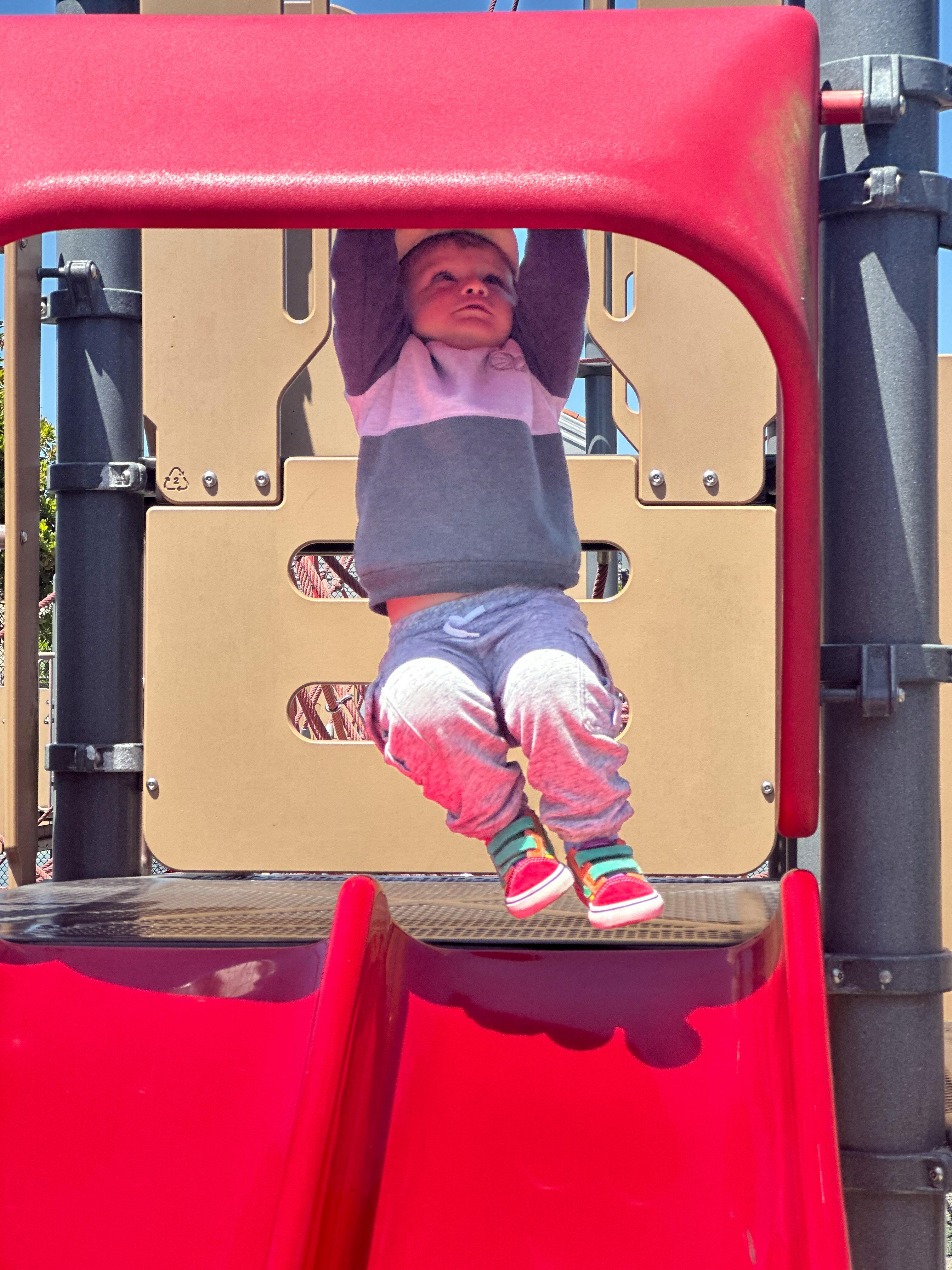 Child on a playground structure, hanging upside down