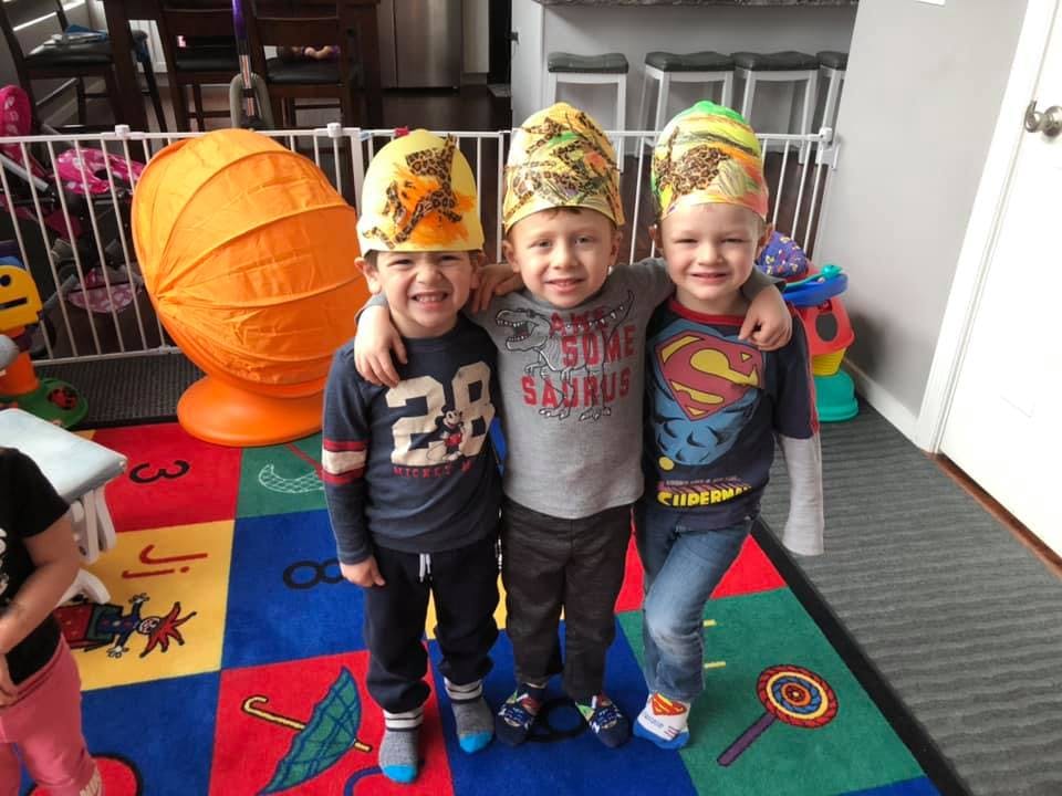 Three children wearing hats standing with arms around each other