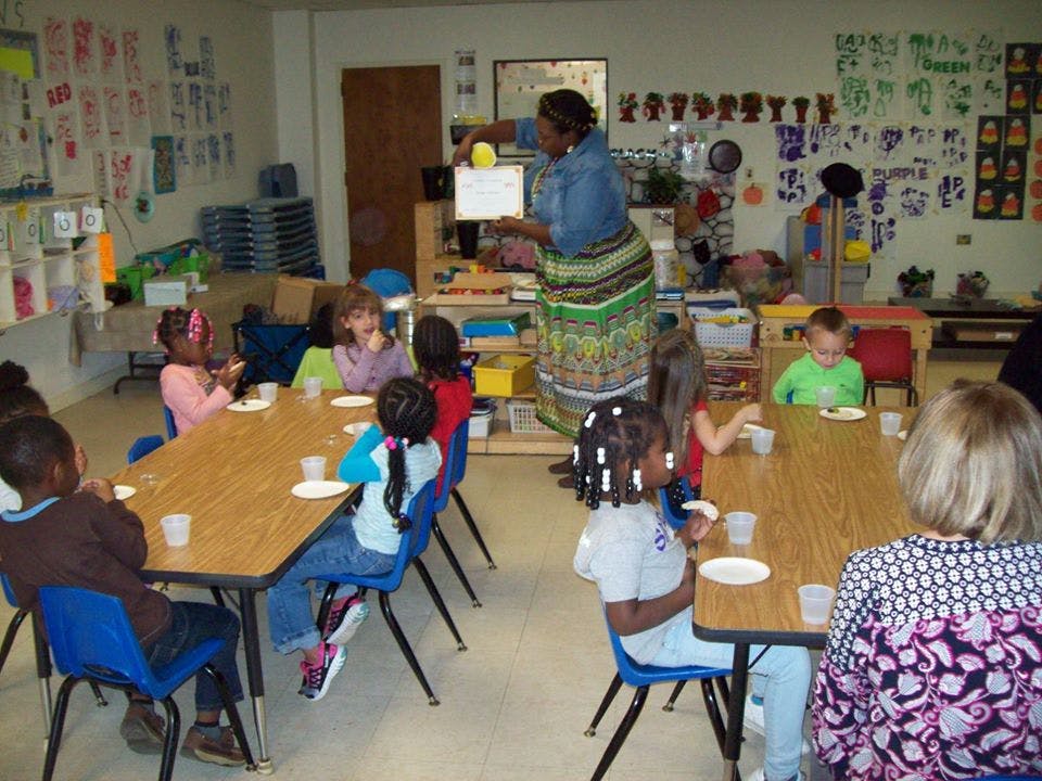 Adult holding a certificate for children seated at tables in a classroom