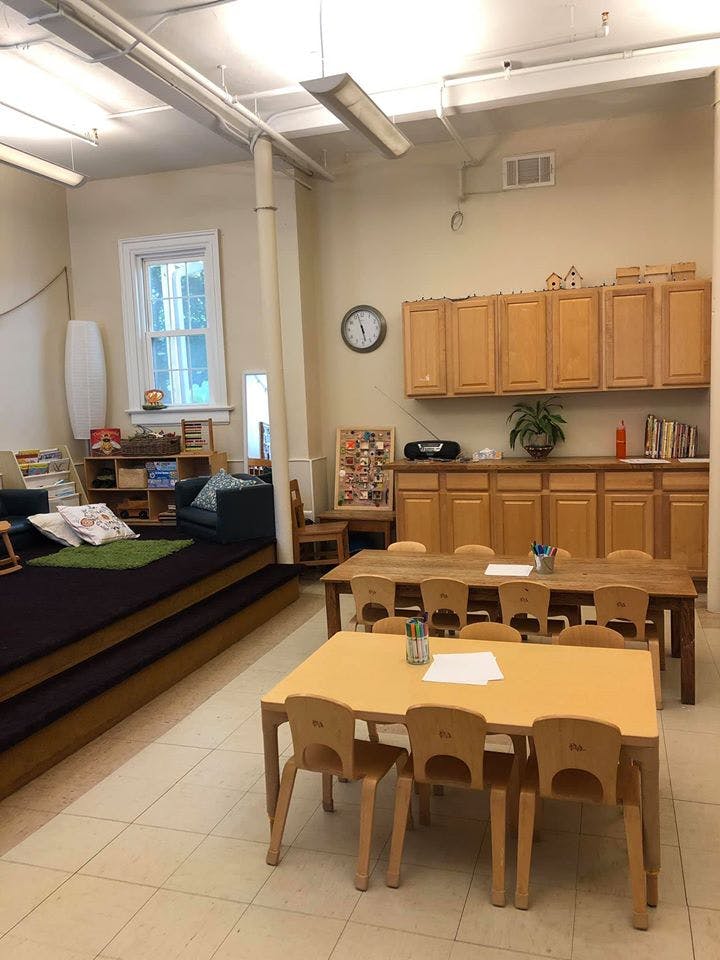 Classroom with small tables and chairs, and a raised platform with cushions