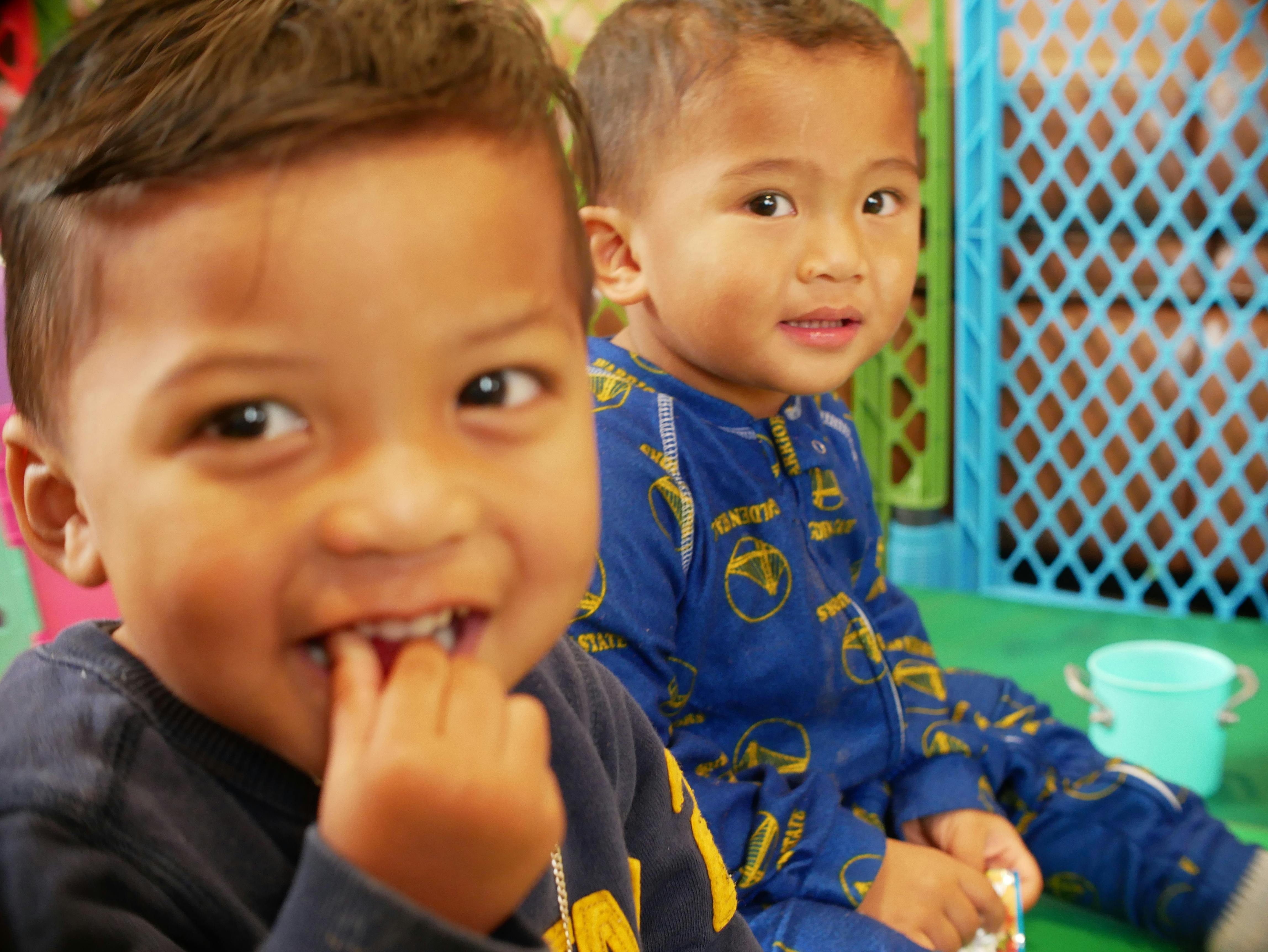 Two children, one in foreground with hand near mouth, one in background