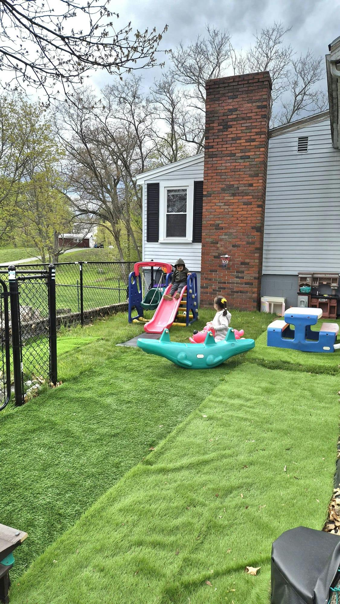 Two children playing on a slide and a seesaw in a grassy yard