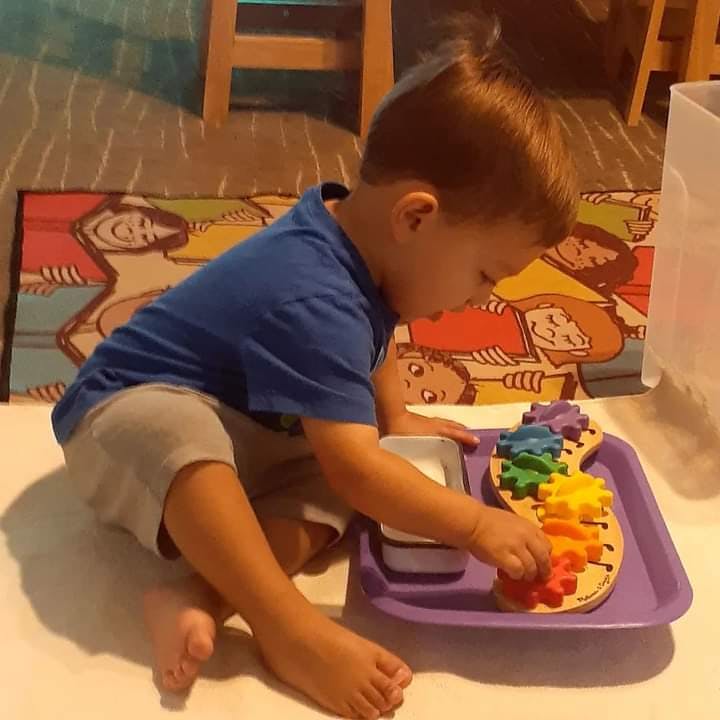 Child playing with a colorful gear toy on a purple tray