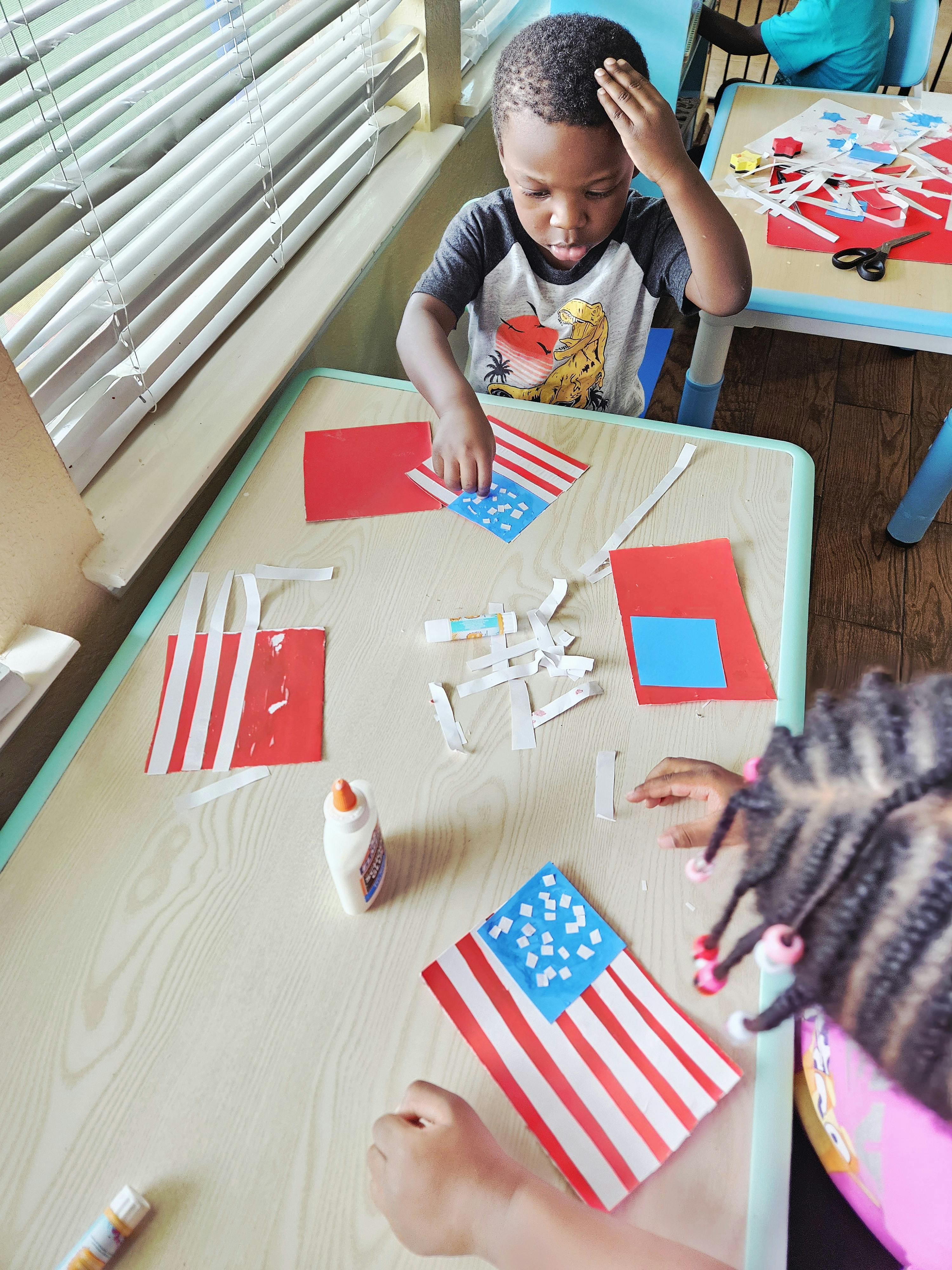 Children working on paper flag craft projects at a classroom table