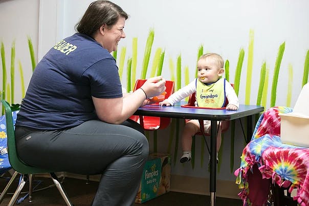 Person feeding a child in a high chair at a table