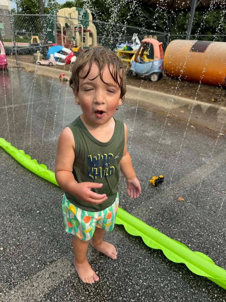 Child standing in water sprinkles at a playground