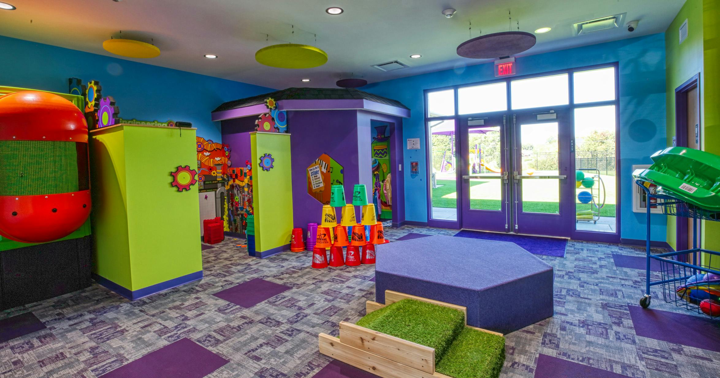 Colorful playroom with green walls, purple accents, and an exit to an outdoor play area