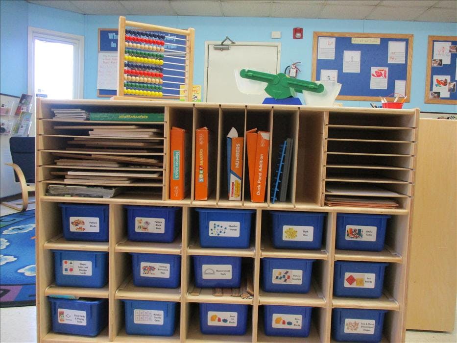 Classroom storage unit with books, papers, and blue bins labeled bins