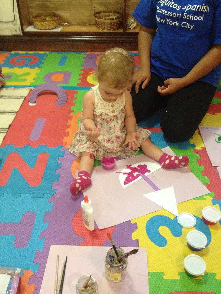Child sitting on a colorful mat, painting on paper