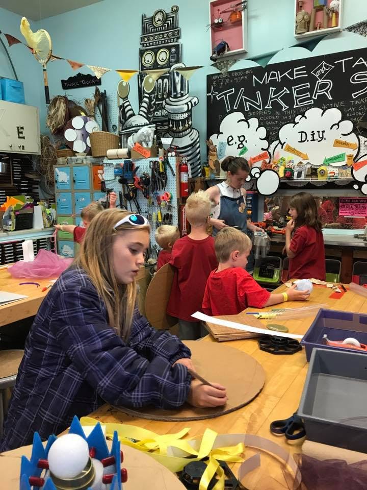 Teen and children working on crafts at tables in a classroom