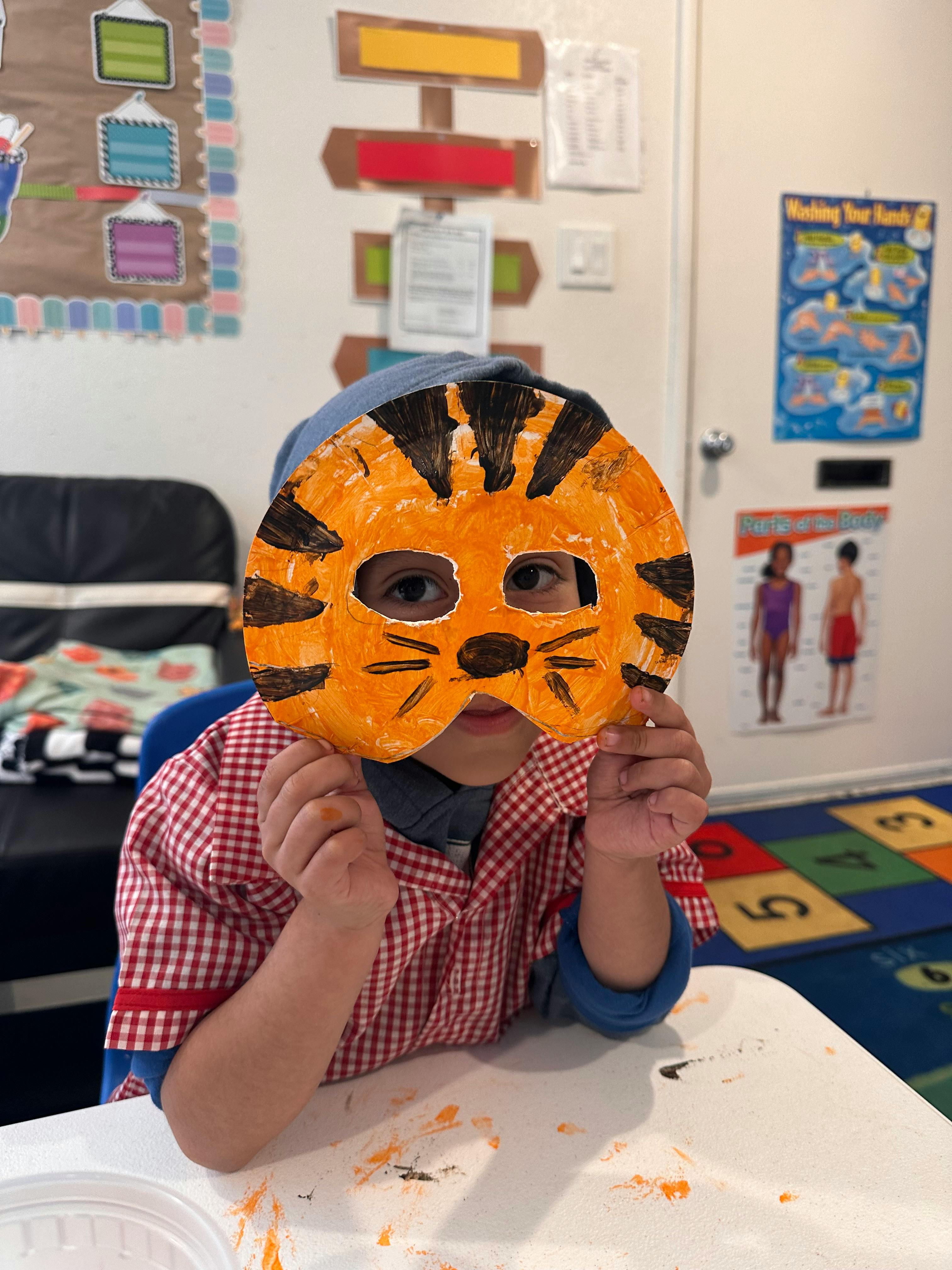 Child holding a tiger mask over their face in a classroom