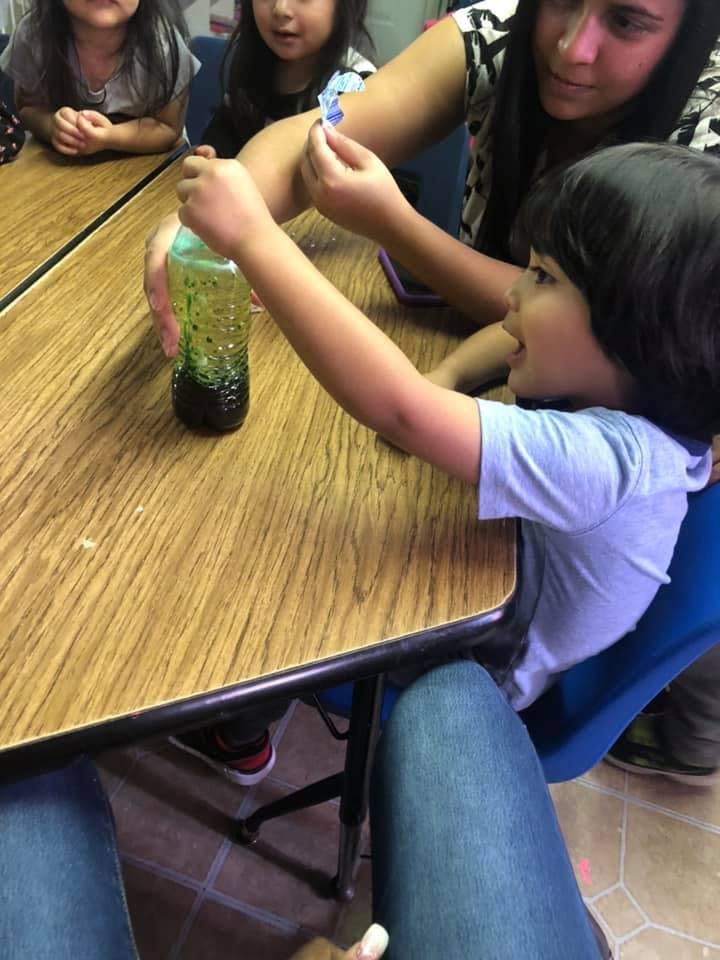 Child holding a bottle with green liquid, person helping