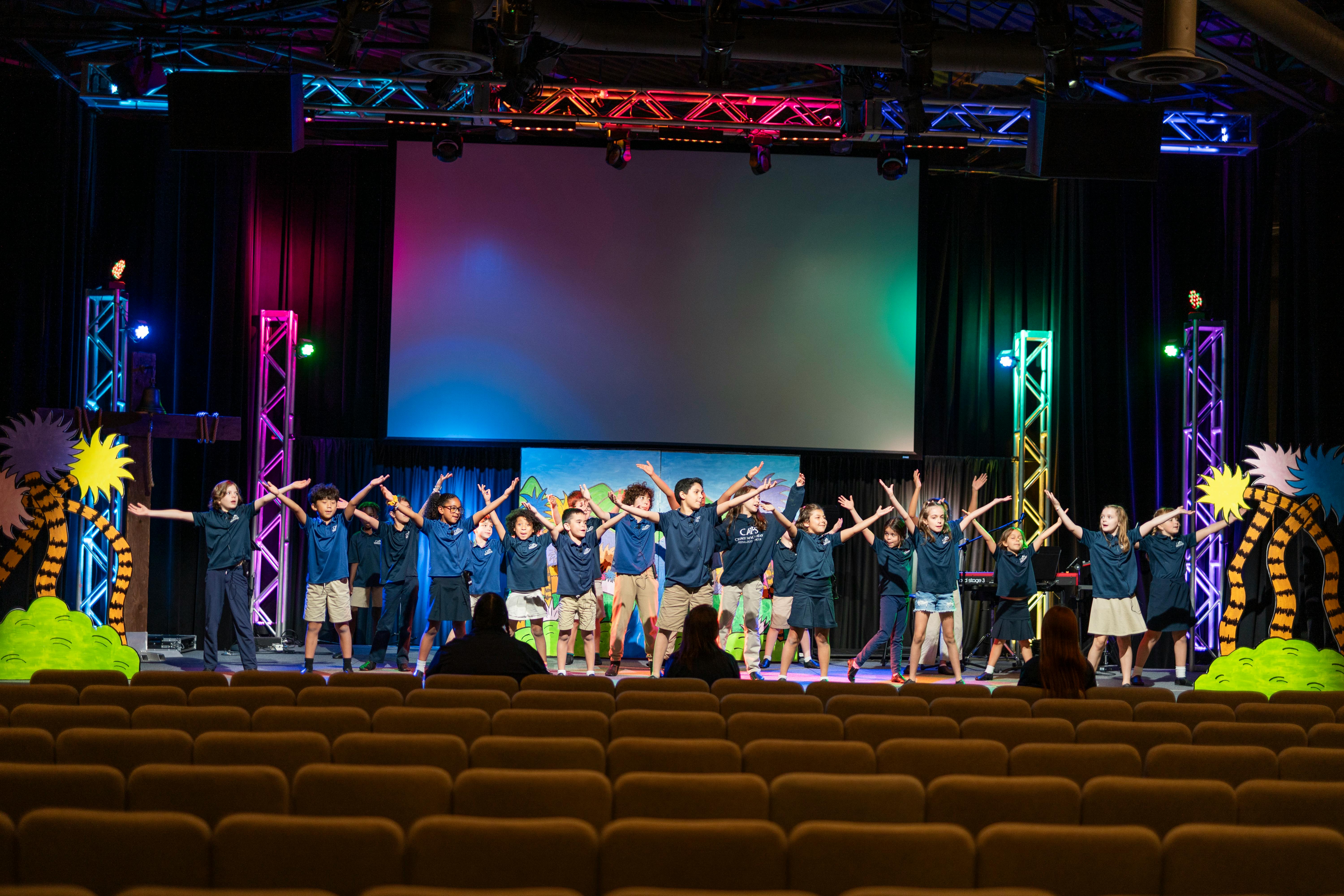 Group of children on a stage with arms raised