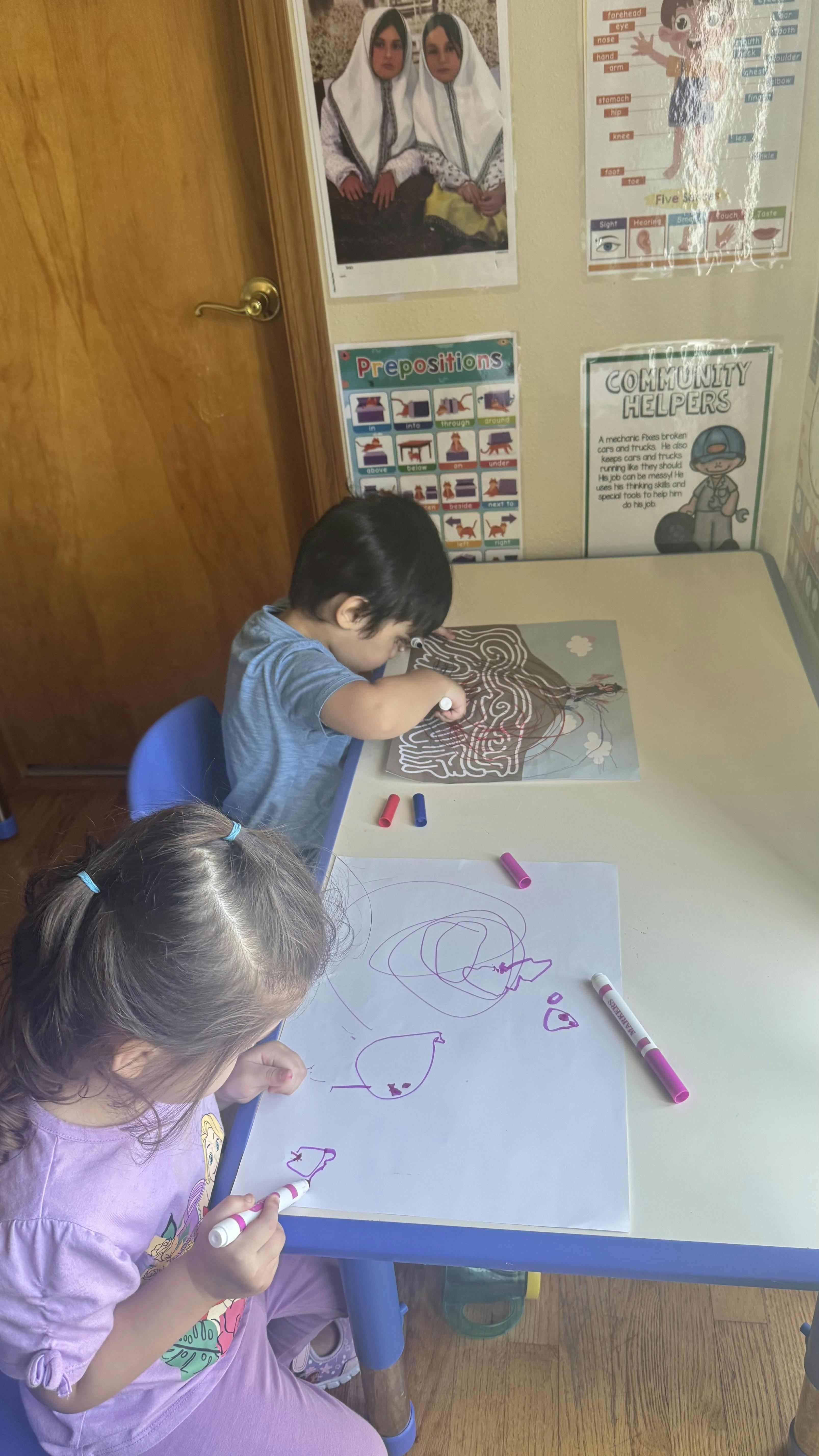 Child drawing with a purple marker next to a child working on a maze