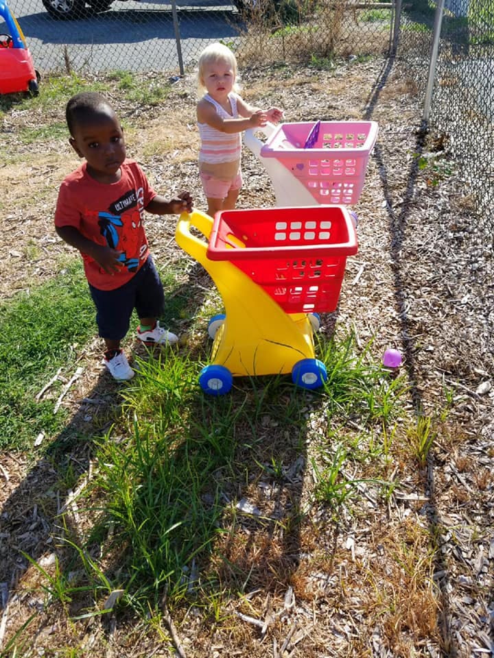 Two children playing with toy shopping carts outdoors