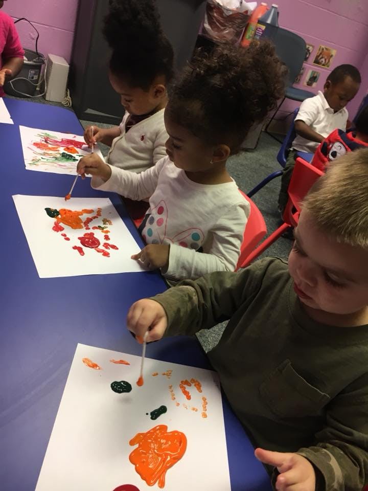Children painting with cotton swabs in a classroom
