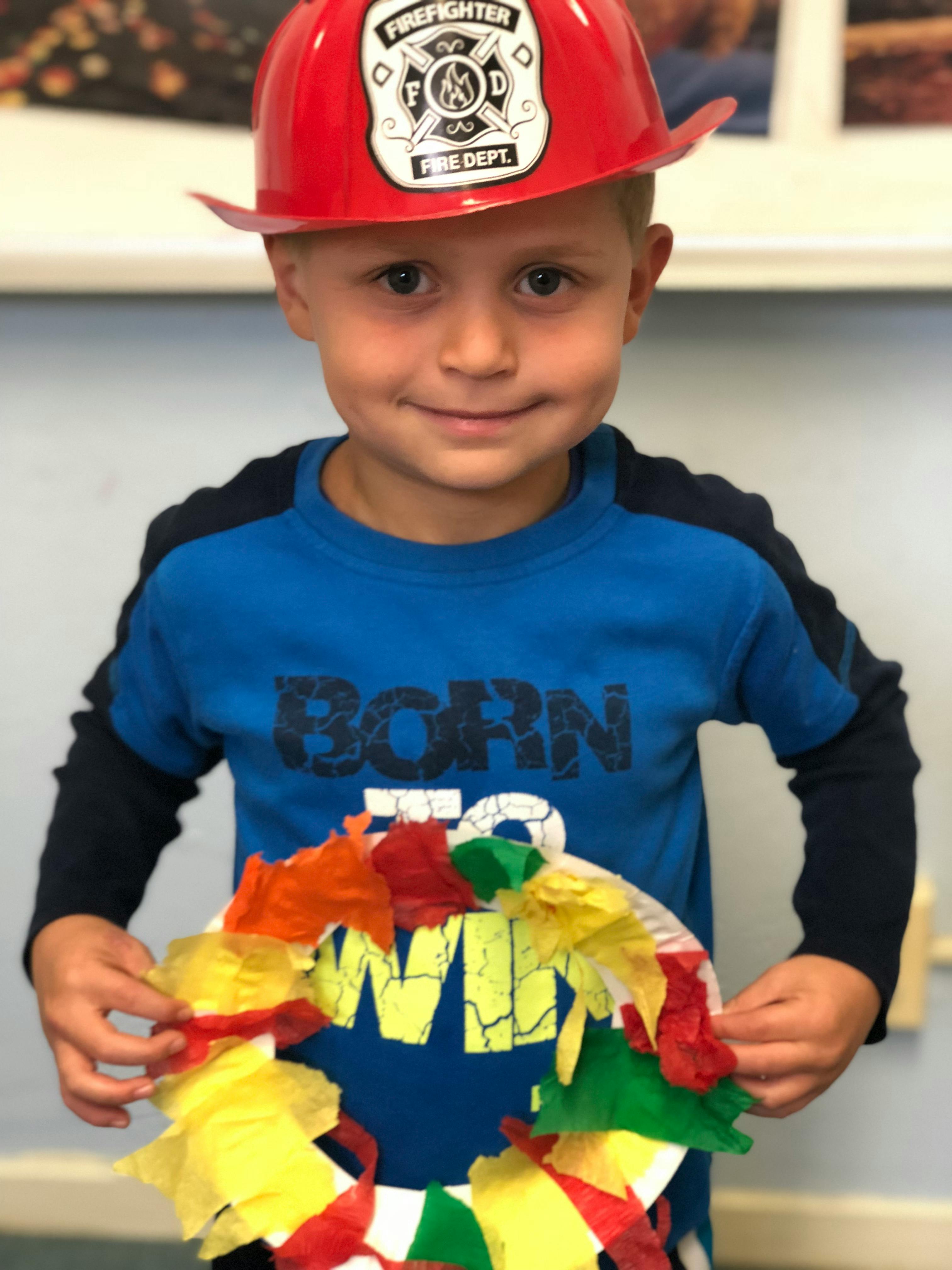 Child in a firefighter hat holding a colorful paper craft