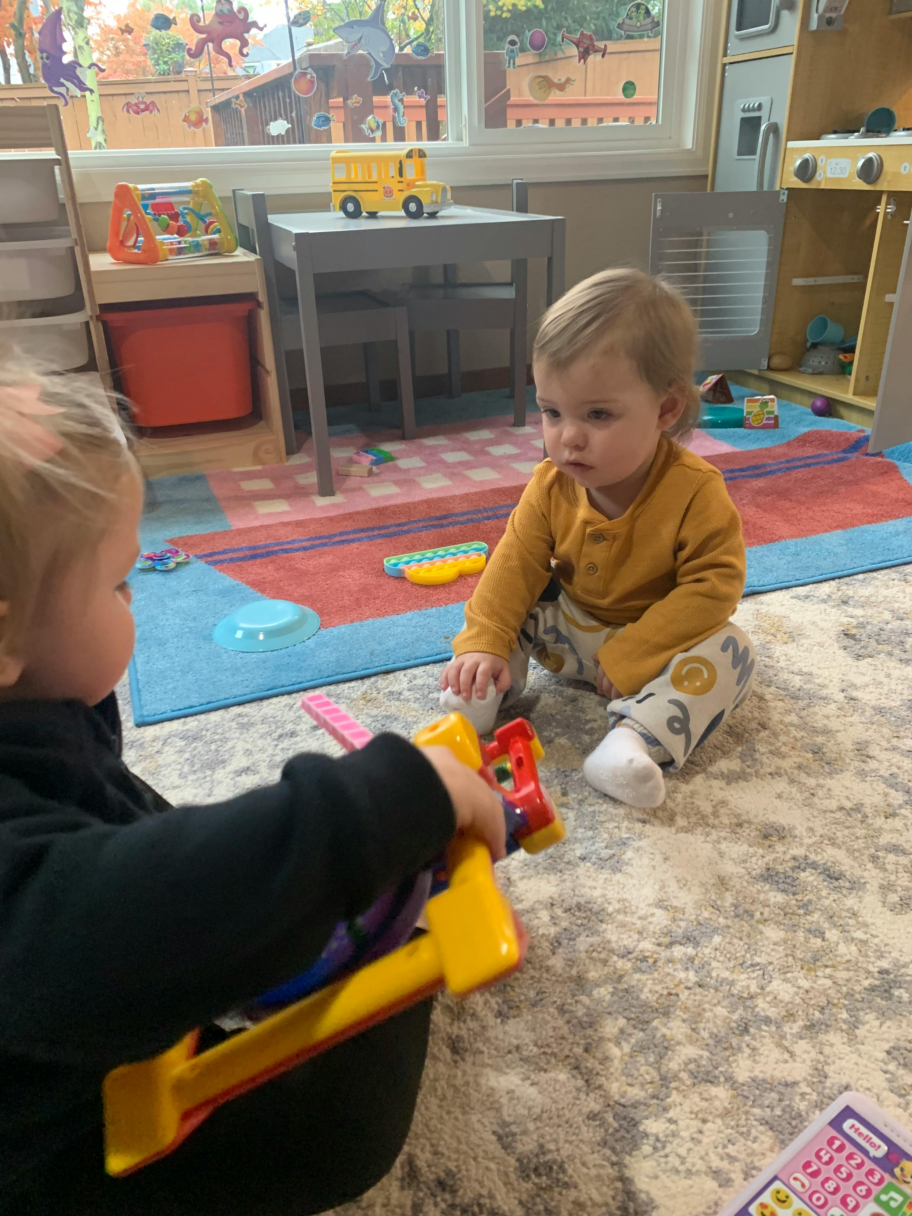 Two children playing with toys on a rug in a classroom